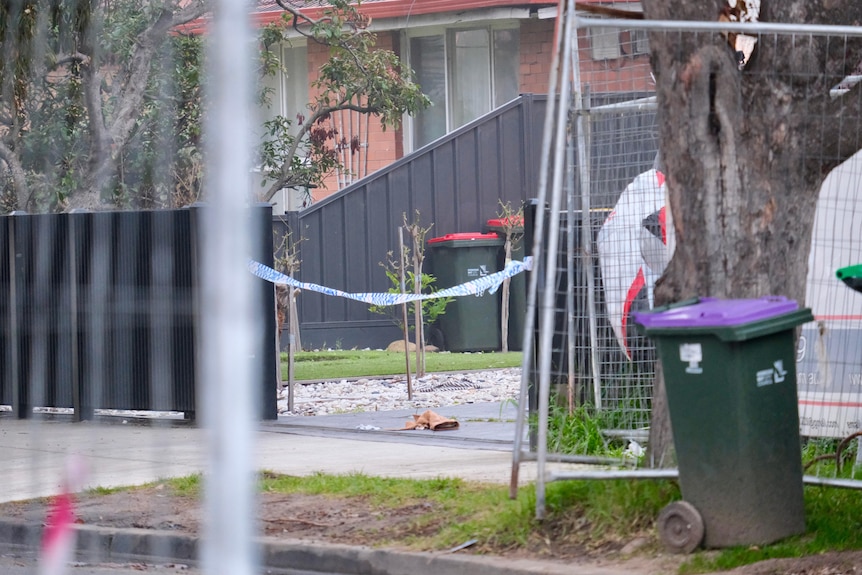 police tape stung up over a suburban driveway surrounded by temporary fencing