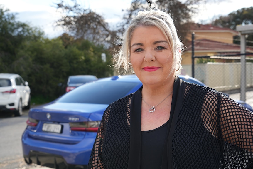 A woman stands in front of a blue car