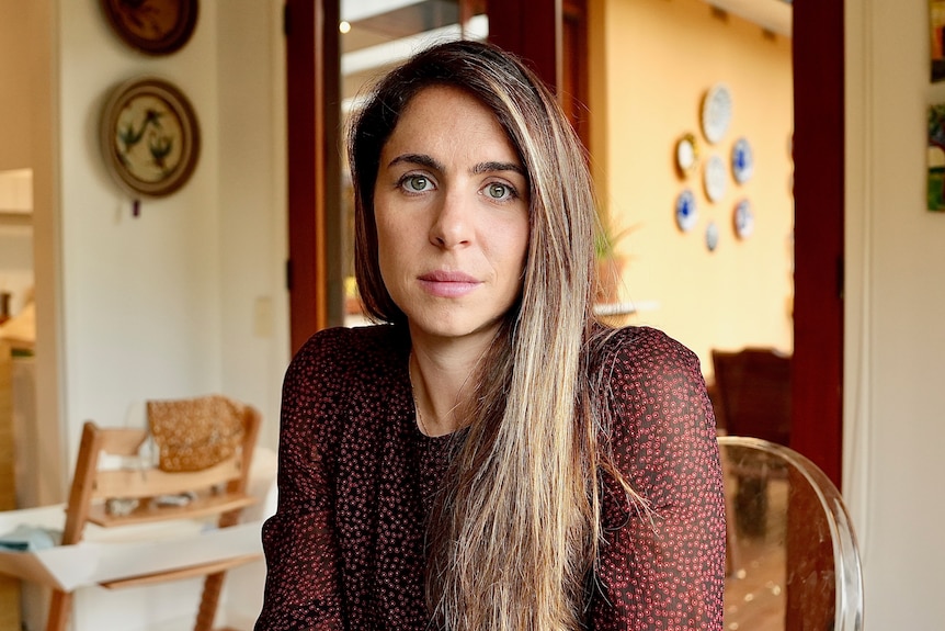Laura Crick sits at a dining table and looks at the camera with a serious expression on her face.