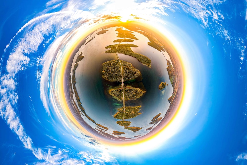 Fisheye shot of a road surrounded by water, circled by sun and clouds.