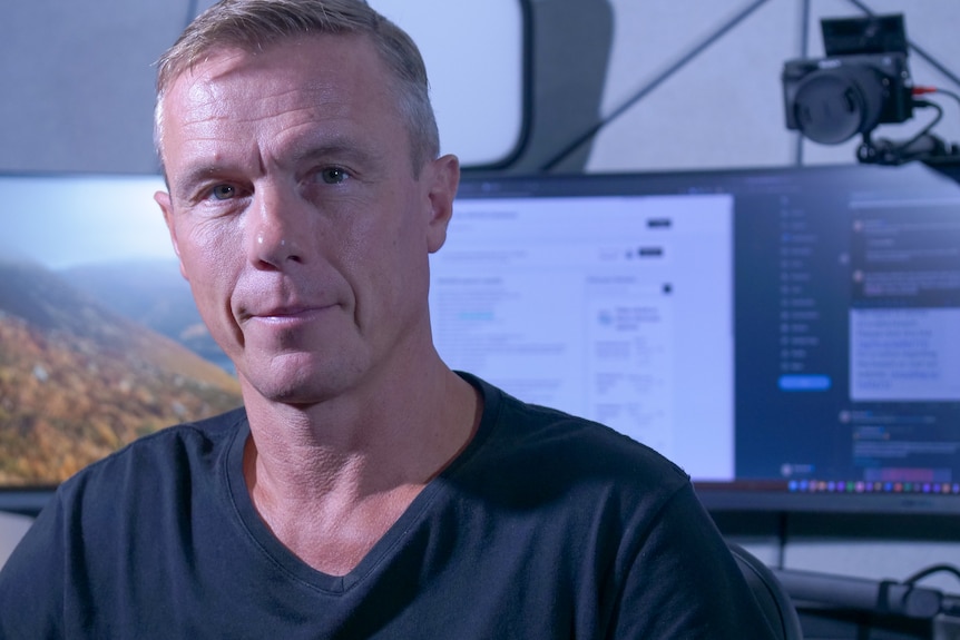 A man in a t shirt sat in front of a computer screen