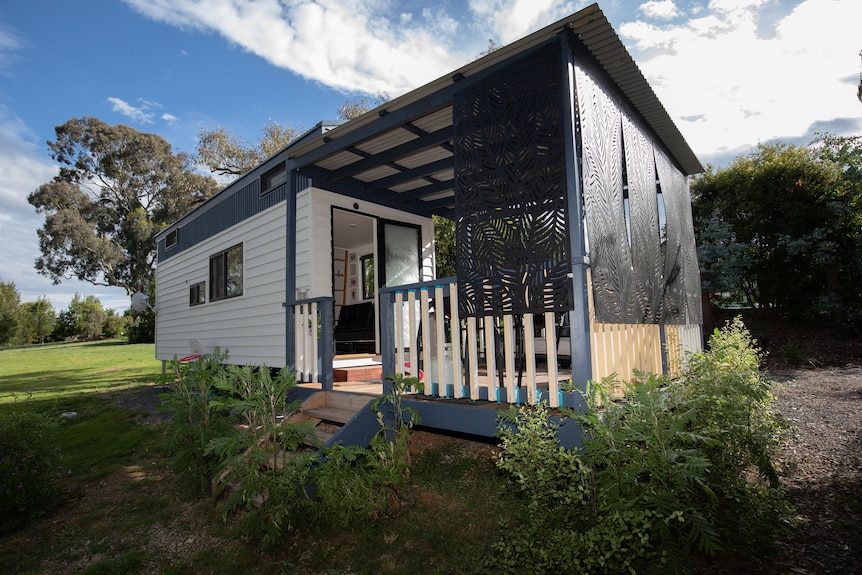A cream and blue coloured granny flat with a patio surrounded by green bushes.
