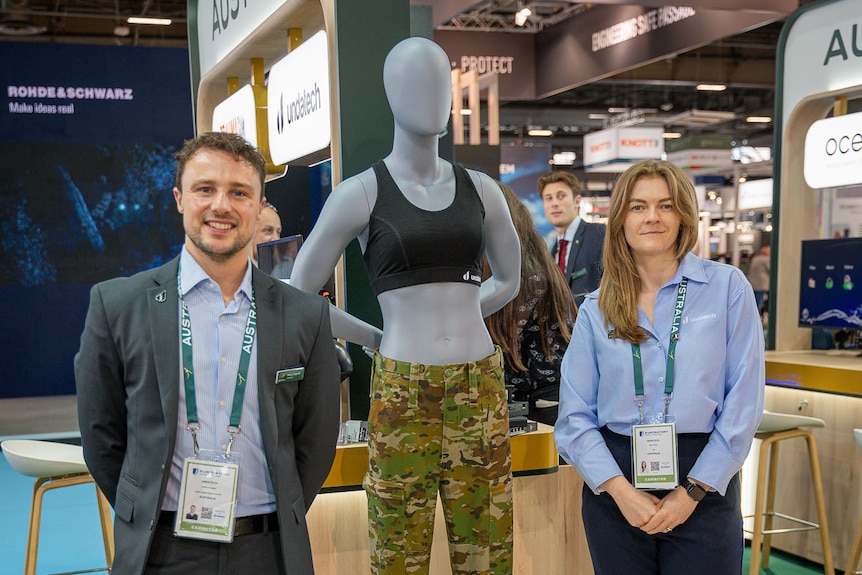 man and woman stand next to a mannequin with a black bra on.