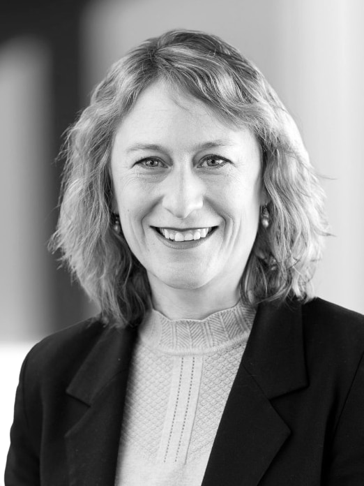A black and white photo of a woman with chin length hair in a blazer smiling at the camera.