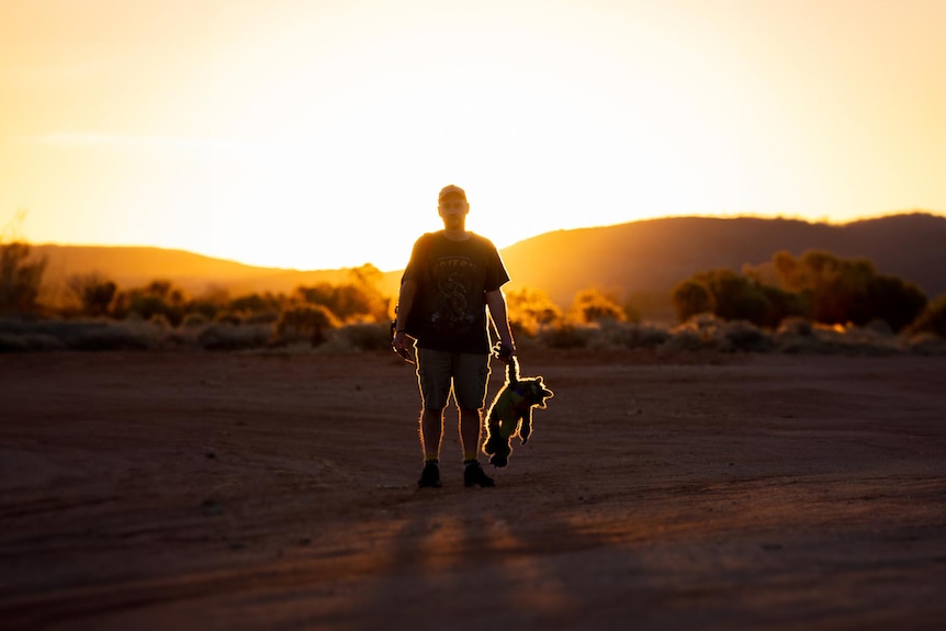 A photo of a person standing in front of a glowing sunset with a small keepsake in his hand.
