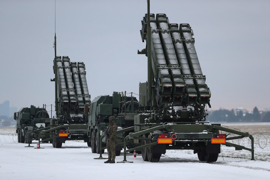 A troop stands next to two air defence systems on wheels