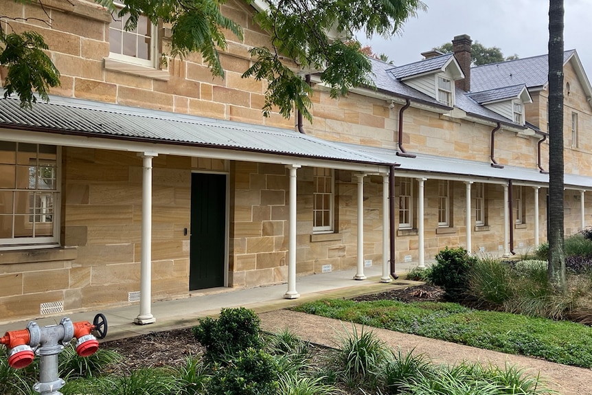 Exterior of sandstone building with white pillars and greenery