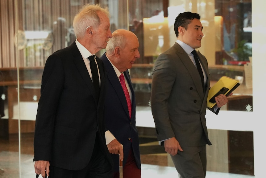 Man in dark blue jacket, white shirt and pink tie walks in other men in suits
