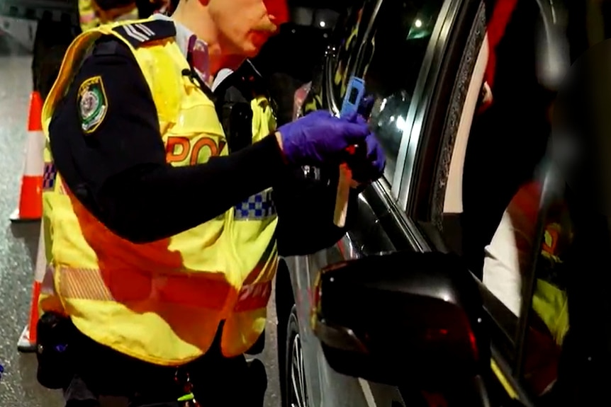 a nsw police officer holds a drug testing device as he explians to a driver at a roadside test the process