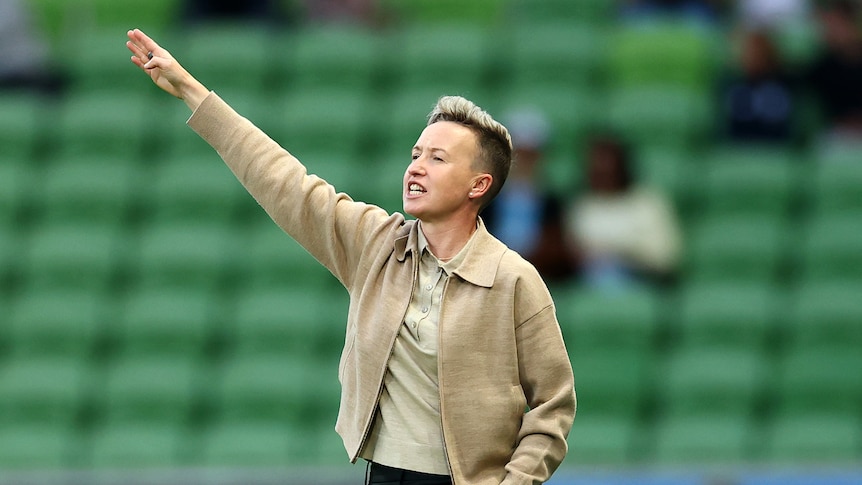 An A-League women's coach holds her arm out to the right to direct players during a grand final.