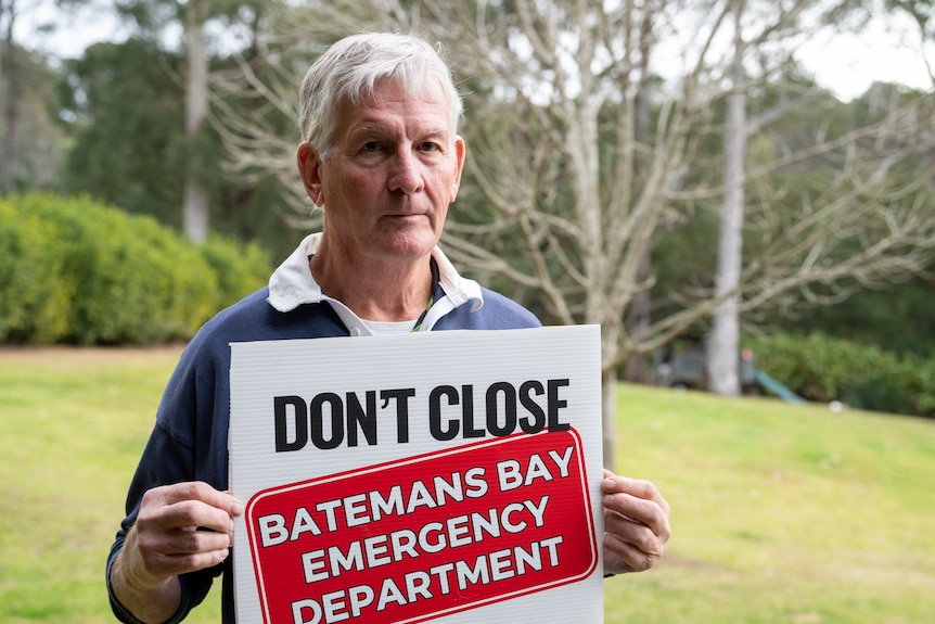 A man holding a sign that says "Don't close Batemans Bay emergency department"