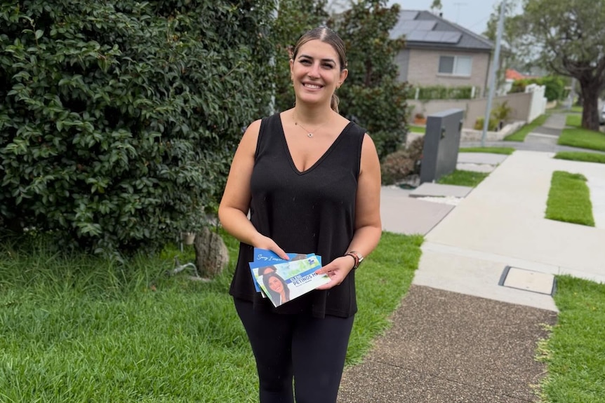 NSW Member for Miranda Eleni Petinos stands on a footpath holding her campaign flyers