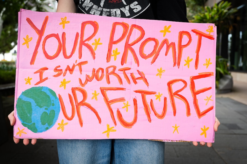 A pink placard hand written by student reading "your prompt isn't worth our future" with the O the planet earth