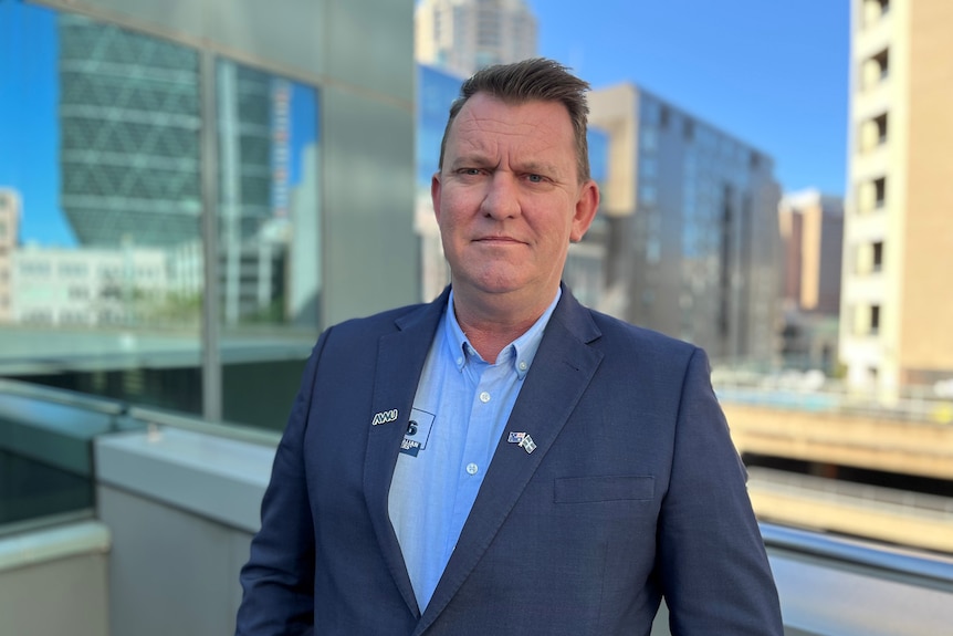 A portrait photo of Paul Farrow on a terrace with highrises in the background