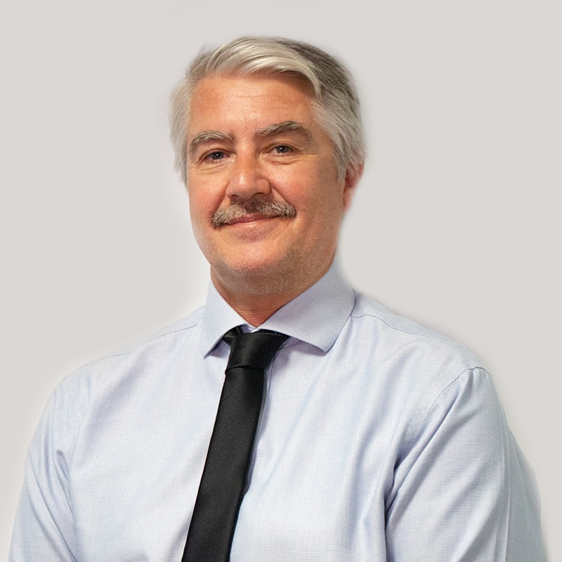 Man with white hair and a moustache smiles at the camera.