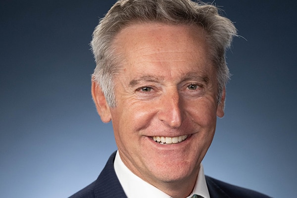 A man in a suit and tie smiles at the camera against a blue background