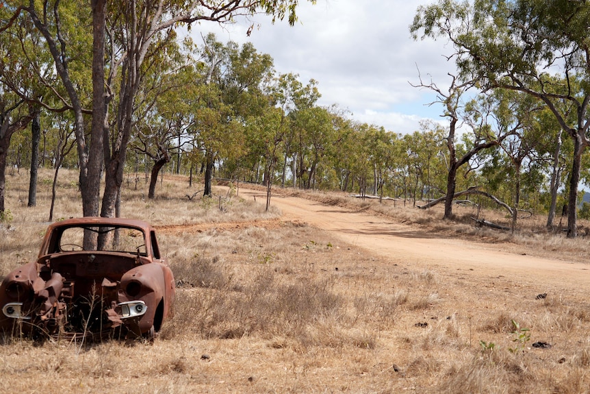 A rusted old car body at the intersection of two dirt roads.
