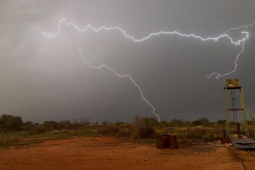 Lightning strikes in bushland with red dirt and a rusty water tower.