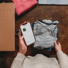 Une femme prépare des vêtements qu'elle va envoyer par colis via une plateforme de vente en ligne.