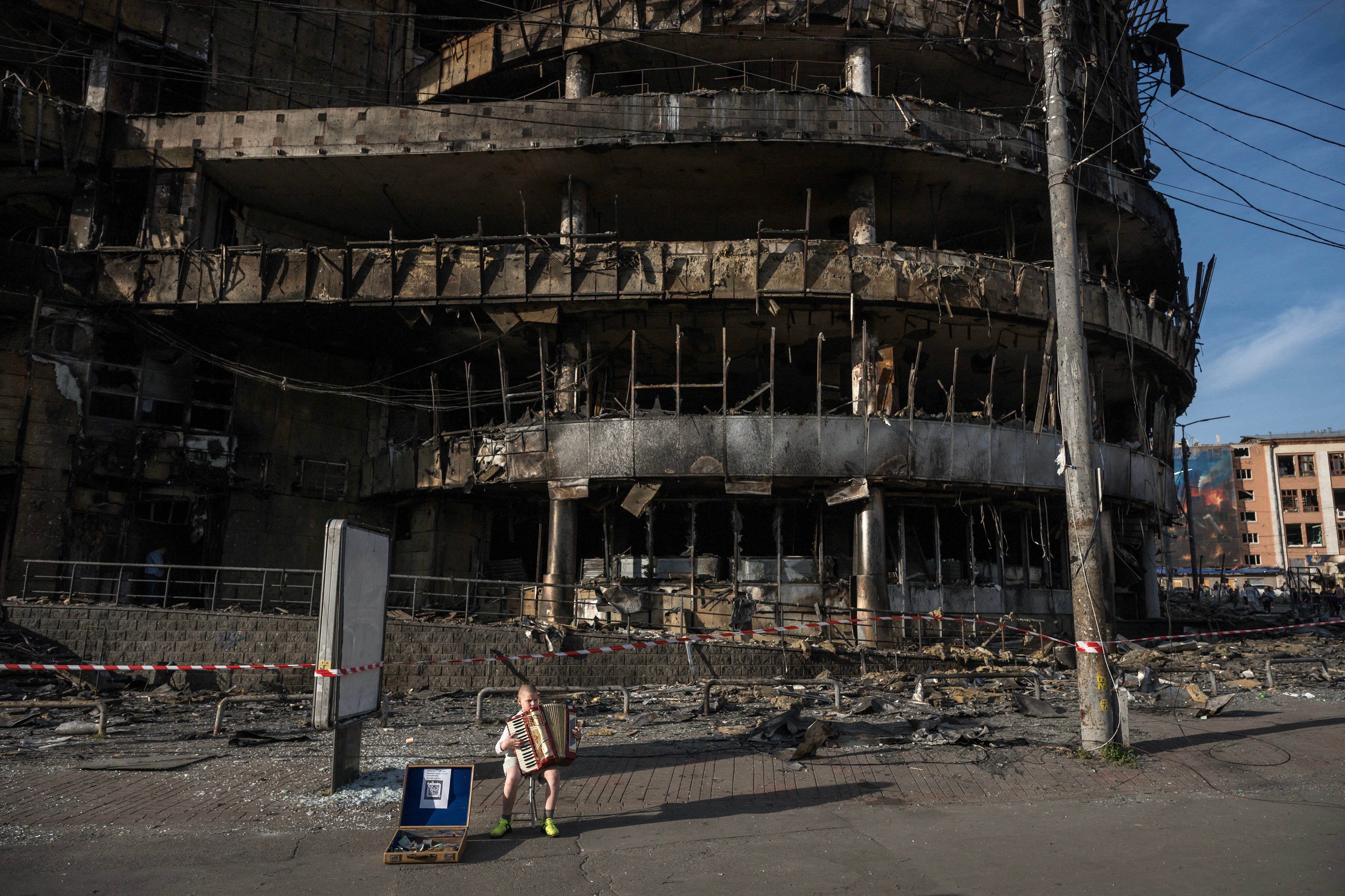 A boy plays the accordion in front of a shopping center damaged by Russian strikes in Kyiv.