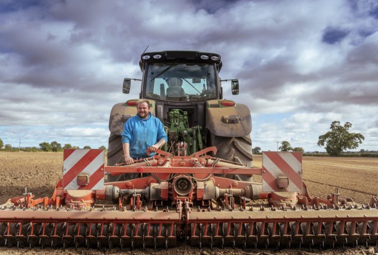 Portrait of smiling farmer at tractor with cultivating plough in plowed field