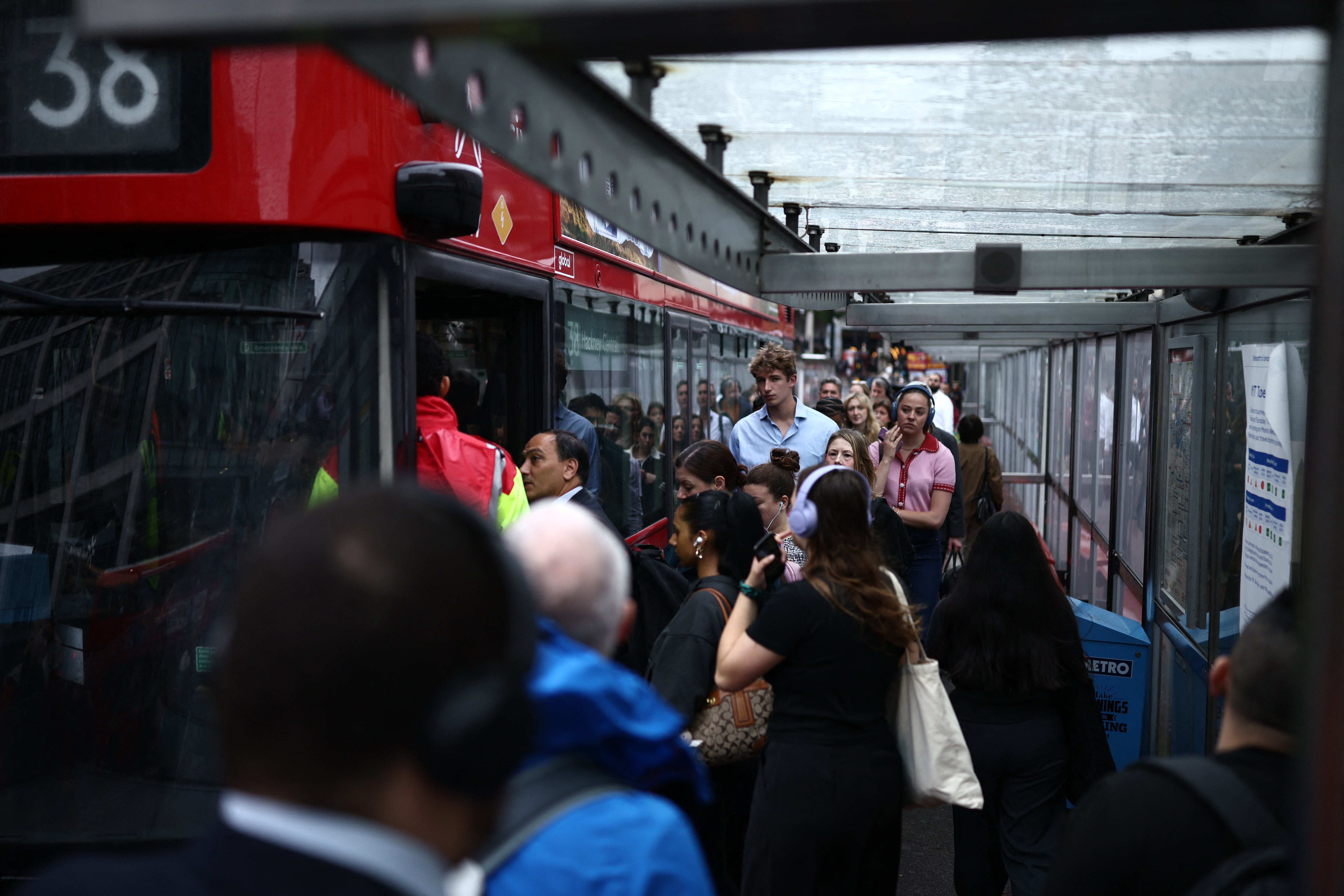 Commuters queue for a red double decker bus outside Victoria train station