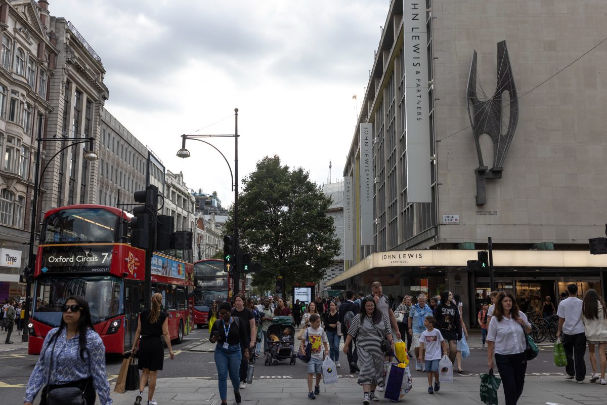 Bustling Oxford Street with shoppers, iconic red buses, and storefronts under a clear sky in a vibrant urban scene
