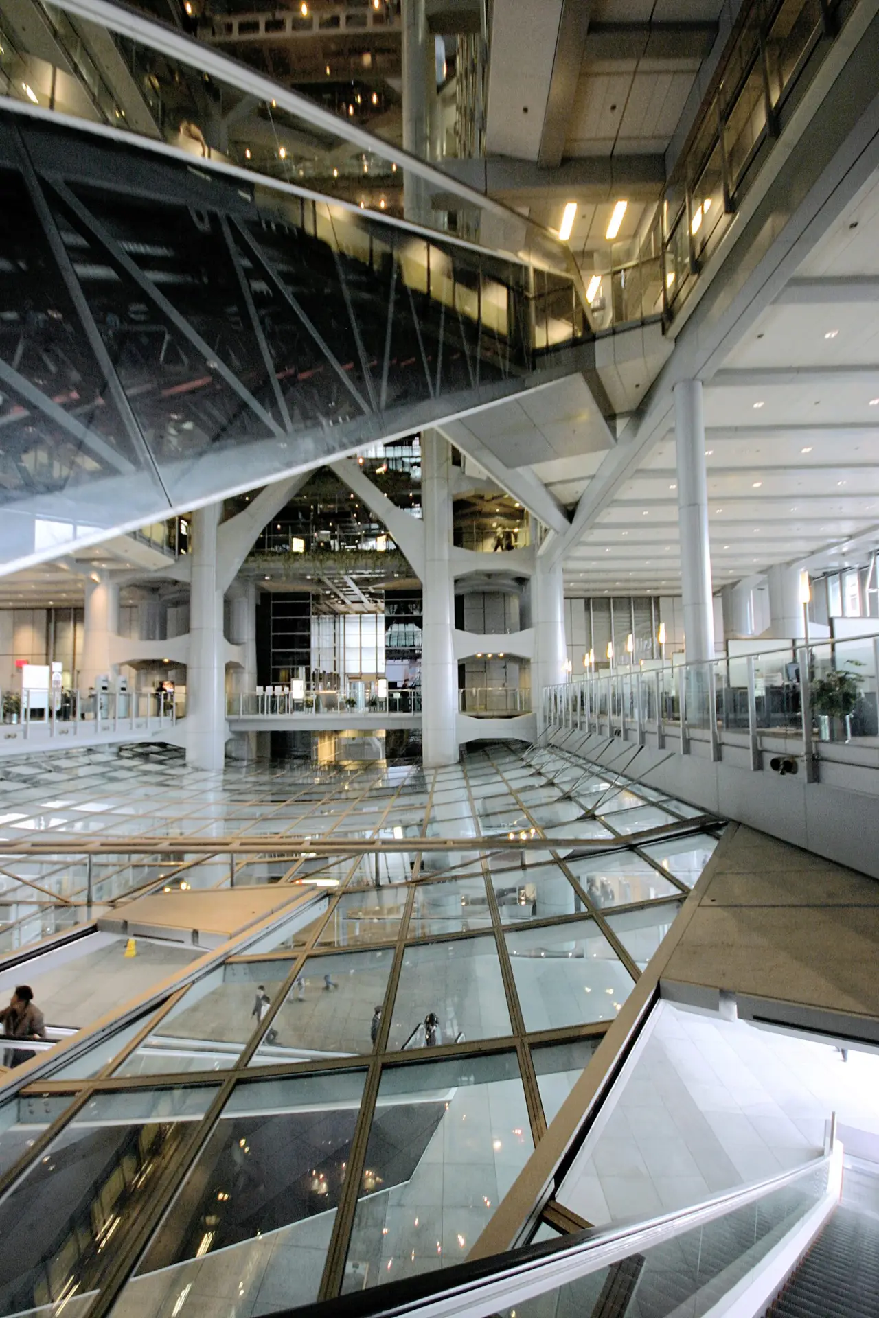 A modern atrium with glass floors, steel beams and curved walkways rises through several levels of a large interior space.