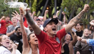 Excited crowd celebrating, a man in an England jersey cheers with arms raised and beer splashing from a cup.