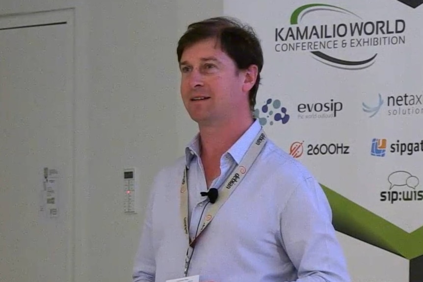 A photo of Daniel Pocock at a conference. He has short black hair, and is wearing a blue shirt.