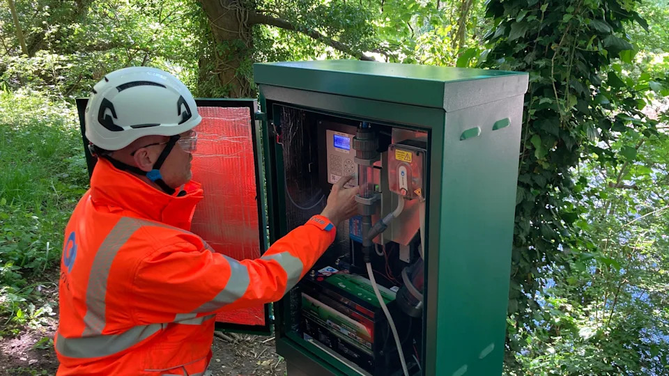 A man looks inside a green, metal cabinet that has been built next to the River Wharfe in Ilkley. Inside are a series of tubes and electronic equipment that extract water from the river.