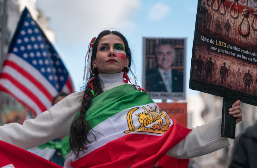 A woman wearing a Lion and Sun Iranian flag (used before the 1980 Islamic Revolution) holds a sign during a protest in solidarity with the anti-government protesters of Iran on February 14, 2026.
