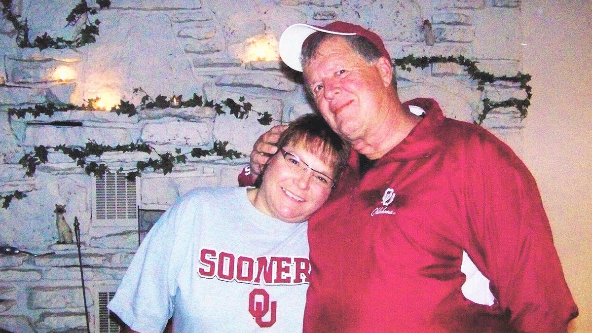 Deb Proctor in a grey college shirt being held by Jeff Walton in a red jacket.