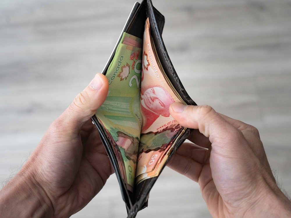 A person&rsquo;s hands can be seen holding a wallet open, showing Canadian $20 bills on one side and $50 bills on the other.