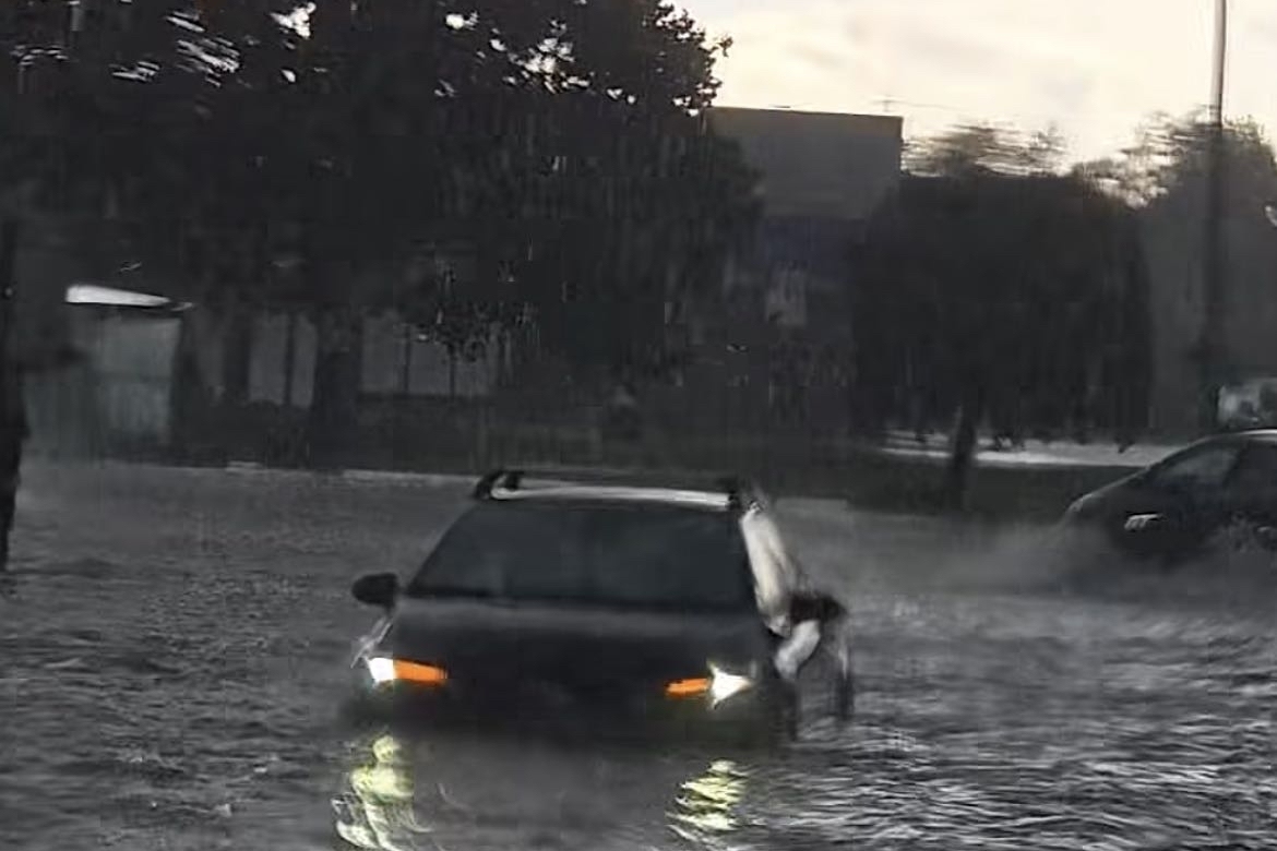 A car is partially submerged on a flooded street.