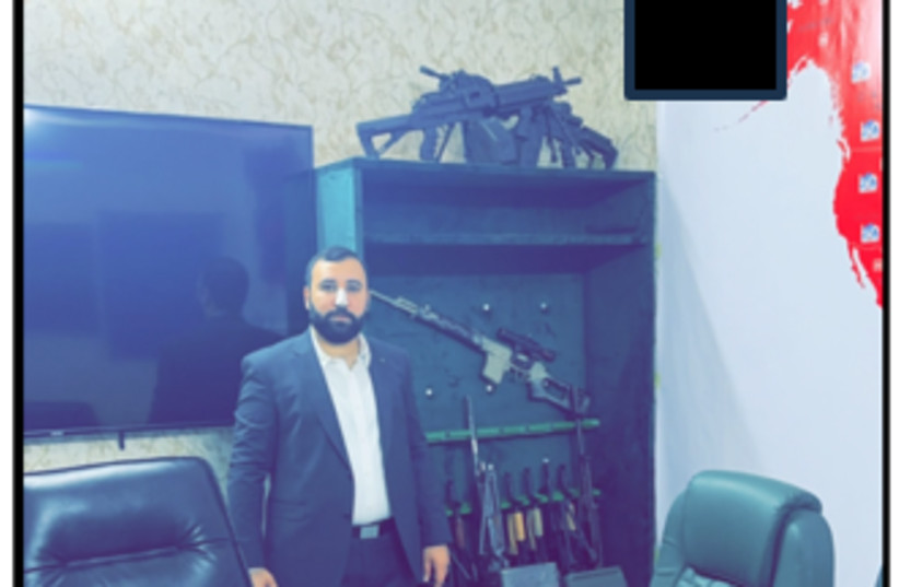 MOHAMMAD BAQER Saad Dawood Al-Saadi standing in front of an array of machineguns in a conference room.