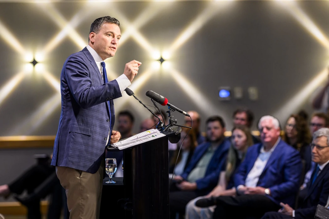 Evan Solomon speaks on stage with bright lights behind him.