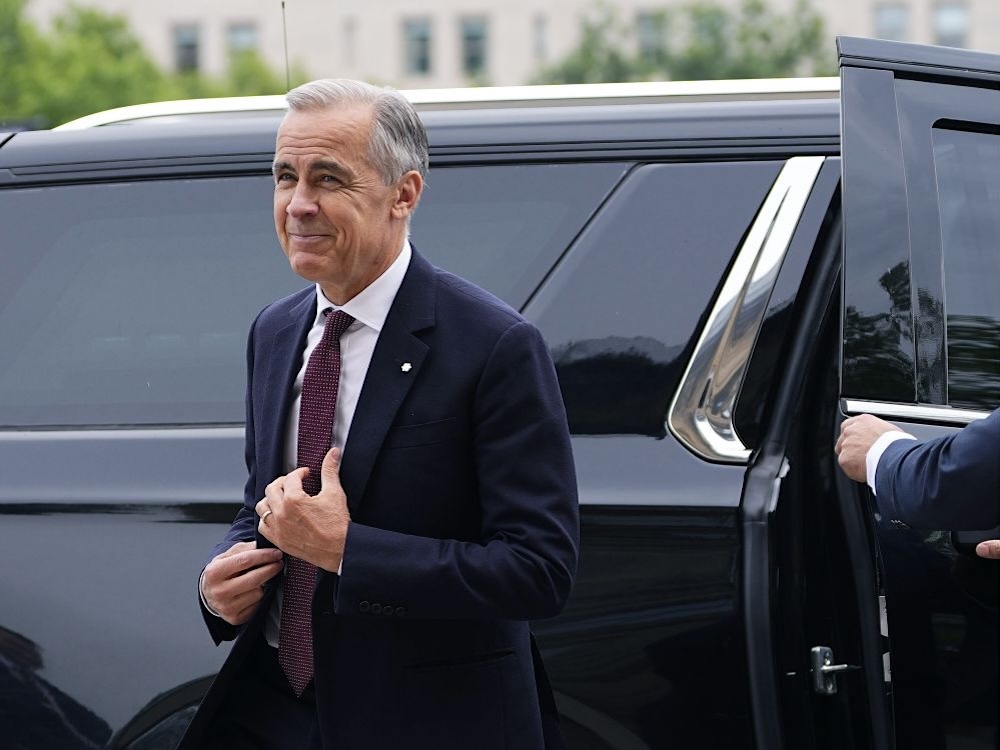 Mark Carney exits a black vehicle. He is wearing a navy blue suit and has a tight-lipped smile on his face.