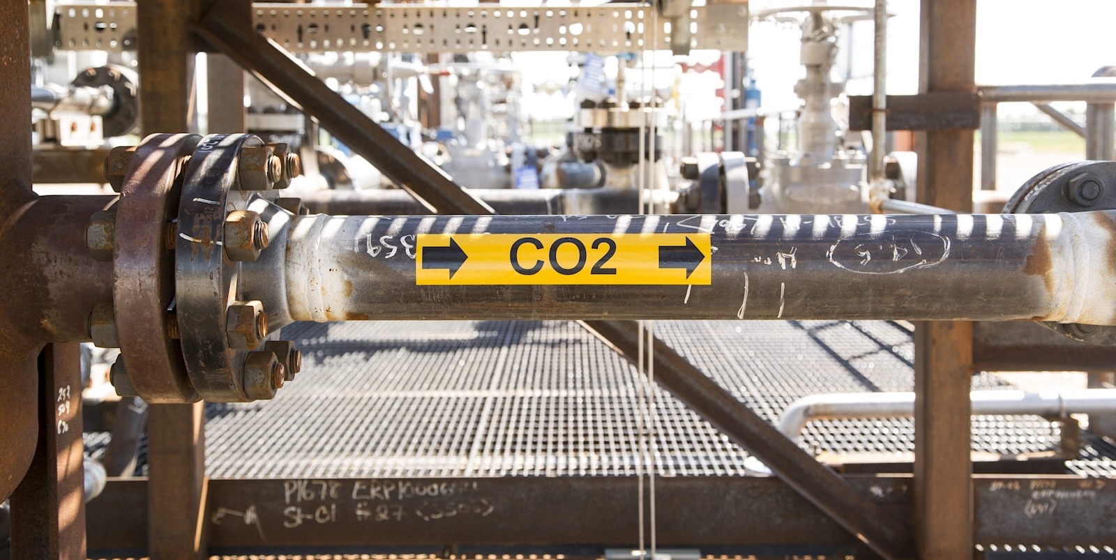A yellow label marked ‘CO2’ with arrows pointing to the right is seen on a pipe in an industrial setting.
