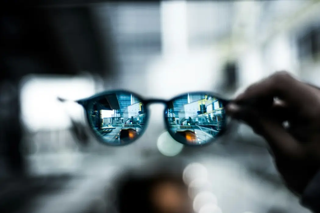 A hand holding smart glasses, viewing a cityscape.