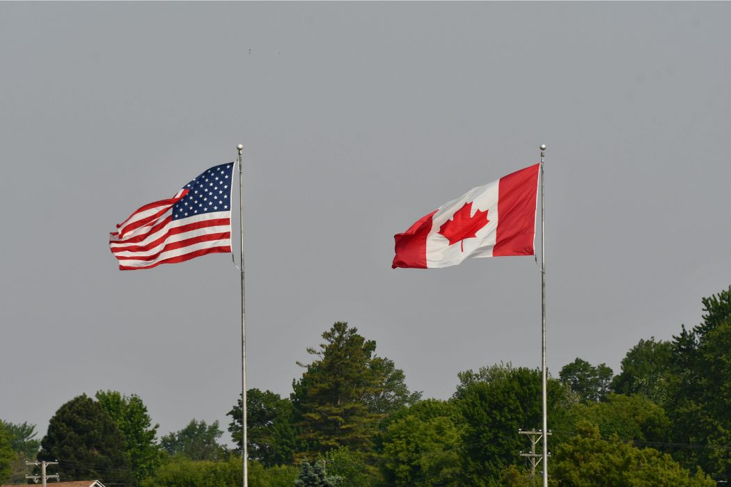 A Canadian and American flag flap in the wind, side by side.