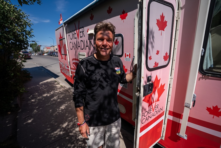 Thomas Lukaszuk stands next to an RV painted with Canadian maple leaves and the words "Forever Canadian".