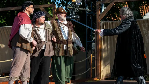 Vier Männer stehen auf einer Bühne und spielen in einem Theaterstück.