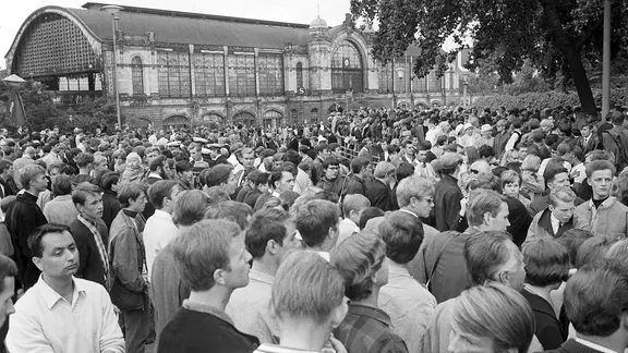 Tausende Jugendliche haben sich am Dammtorbahnhof versammelt, um zum Konzert zu gelangen. | picture alliance / dpa | Werner Reuss Tausende von Jugendlichen versuchen am 26.06.1966 den Eingang zum Ausstellungsgelände Planten un Blomen in Hamburg zu stürmen. Grund: In der Ernst-Merck-Halle treten die Beatles auf.