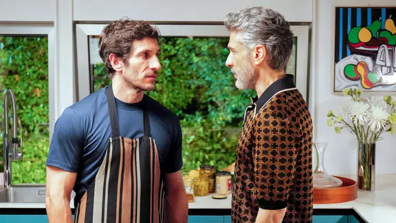 Leonardo Sbaraglia (r.) als Raúl und Quim Gutiérrez als Santi in einer Szene aus "Bitteres Fest" | StudioCanal/dpa Ein Mann mit Kochschürze und ein anderer Mann stehen sich in einer Küche gegenüber.