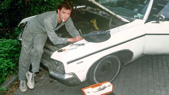 Der deutsche Schauspieler Jan Fedder repapariert einen US-Straßenkreuzer, aufgenommen 1991 in Hamurg. | picture alliance / Stefan Hesse , Stefan Hesse Der deutsche Schauspieler Jan Fedder repapariert einen US-Straßenkreuzer, aufgenommen 1991 in Hamurg.