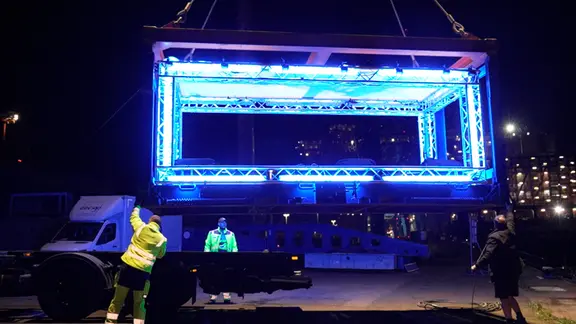 Auf dem Hafengeburtstag gab es das erste sichtbare Zeichen des diesjährigen Blue Port. | NDR/ADAMFilm Ein blau beleuchtetes Gerüst wird von einem Kranwagen gehoben.