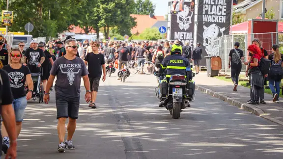 Wacken: Ein Polizeibeamter fährt während des Wacken Open Air (W:O:A) mit einem Motorrad durch die Ortsmitte. | dpa-Bildfunk Wacken: Ein Polizeibeamter fährt während des Wacken Open Air (W:O:A) mit einem Motorrad durch die Ortsmitte.