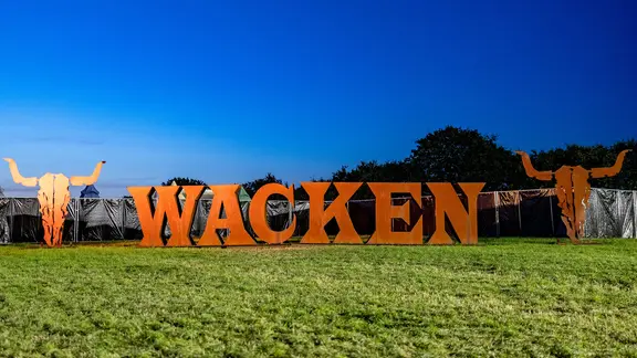 Wacken: Das Festival-Logo gefertigt aus großen Metallbuchstaben, steht auf einer Wiese. | dpa, Axel Heimken Wacken: Das Festival-Logo gefertigt aus großen Metallbuchstaben, steht auf einer Wiese.