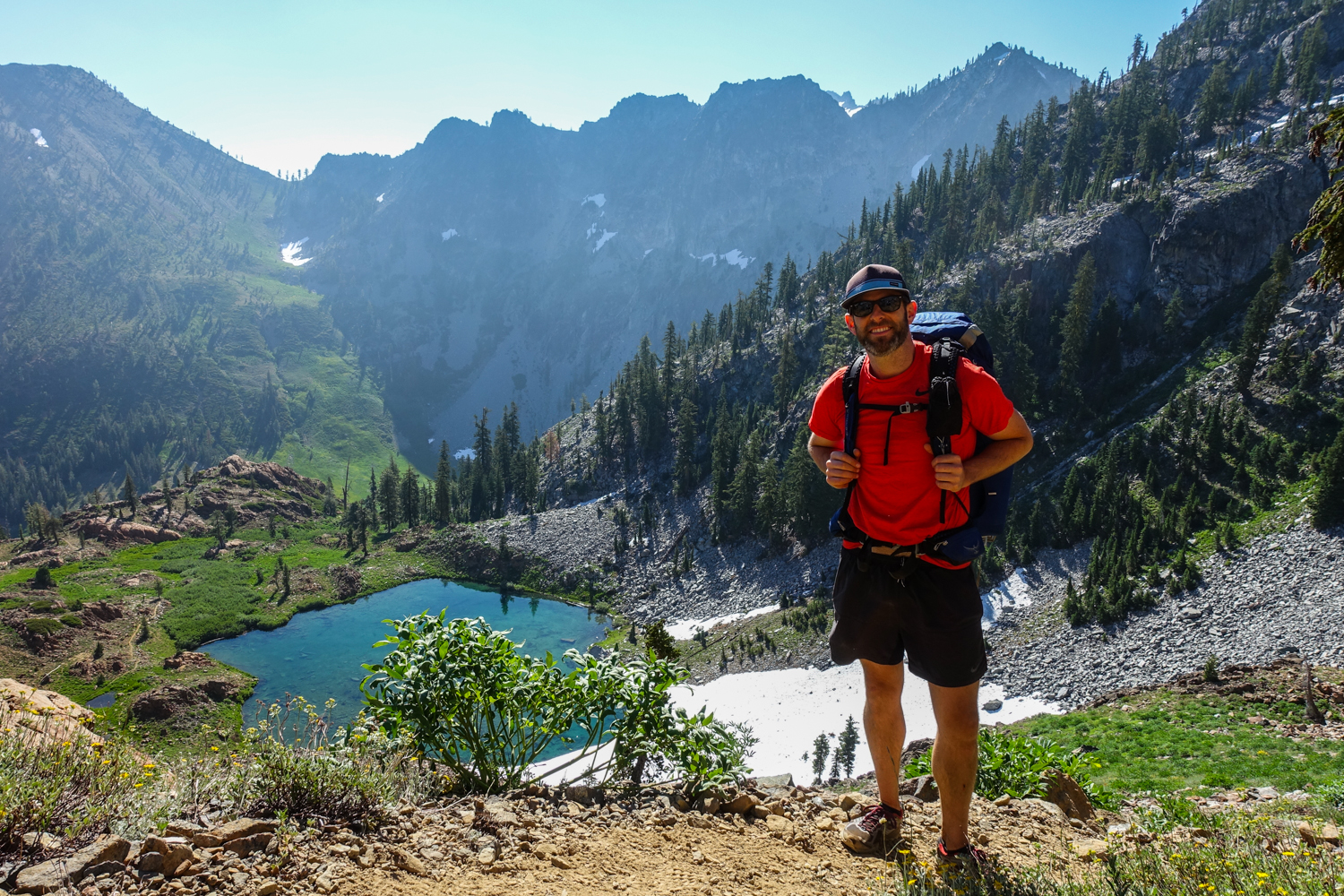 backpacker posing above a blue alpine lake snow on the north side of the lake in the trinity alps